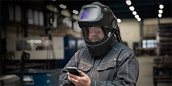 worker wearing a welding helmet looking at a mobile device
