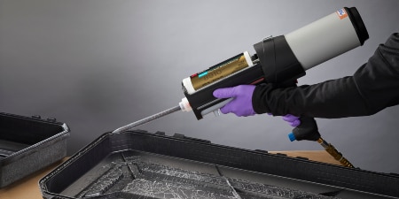 A worker uses a pneumatic applicator to apply the adhesive to a plastic part
