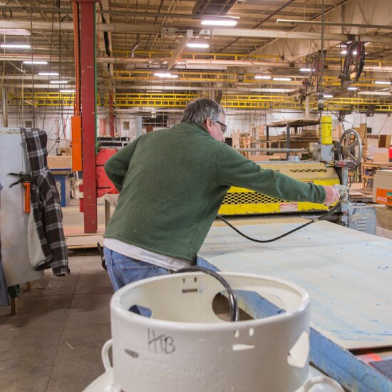 Man applying a 3M™ sprayable adhesives to the surface of a large wooden sheet.