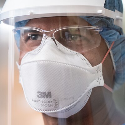 A closeup of a person wearing a 3M faceshield, disposable respirator and protective eyewear
