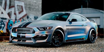 metallic car with a race stripe in front of a graffiti building
