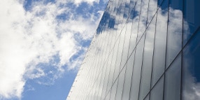 Exterior photo looking up at glass wall building against blue sky with clouds
