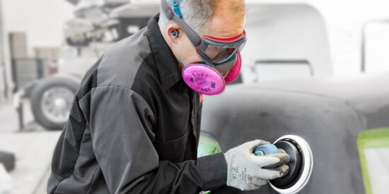 Man in a protective respirator sanding the body of a vehicle.
