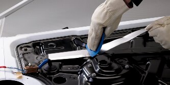 A worker applies a damping foil tape to a metal frame to help damp vibration and noise
