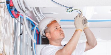 An electrician in a hard hat wiring lights in the ceiling.