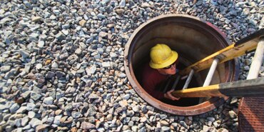 An electrician in a yellow hard hat descending a ladder into a confined space.