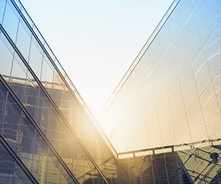 Bright sun shining over angular window-covered buildings
