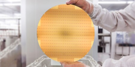 Hands holding a gold colored semiconductor wafer
