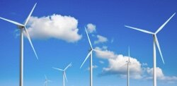 Five wind turbines with a cloud speckled blue sky in the background.
