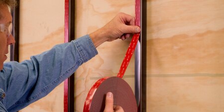 Image of a worker applying 3M™ VHB™ Tape to a series of vertical frame bars before adding a panel
