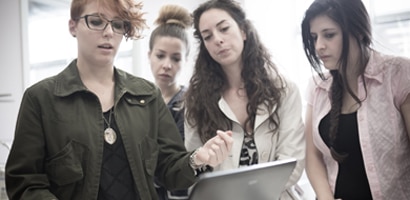 Four people gathered around a laptop computer look at the screen.
