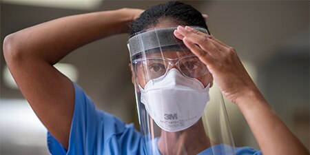 A healthcare clinician secures a faceshield over their head
