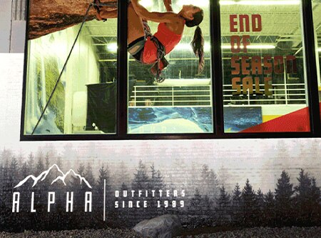 Exterior of retail store at night with printed window graphics and retroreflective film on brick printed with tree motif and logo.
