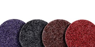 A set of four circular abrasive pads in different colors: purple, black, brown, and red, arranged in a row from left to right.

