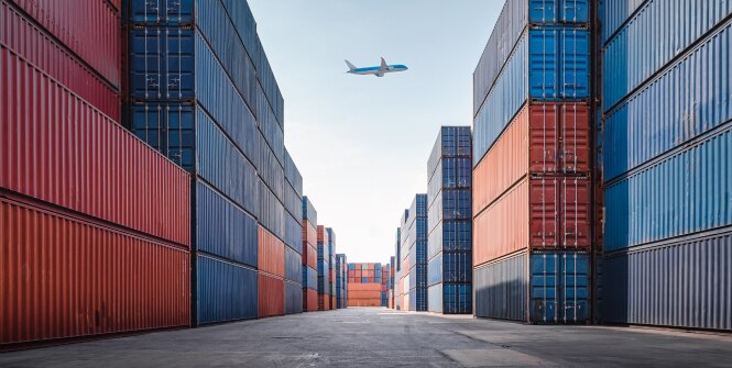 Shipping containers are stacked in rows, creating narrow pathways between them.
