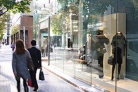 People walking though an outdoor shopping mall by a glass display