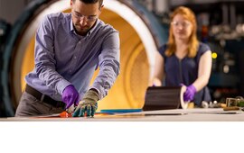 Man measuring a roll on a table with a woman holding the roll at the other end of the table.