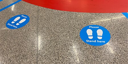 A downward looking shot of a floor with social distancing graphics
