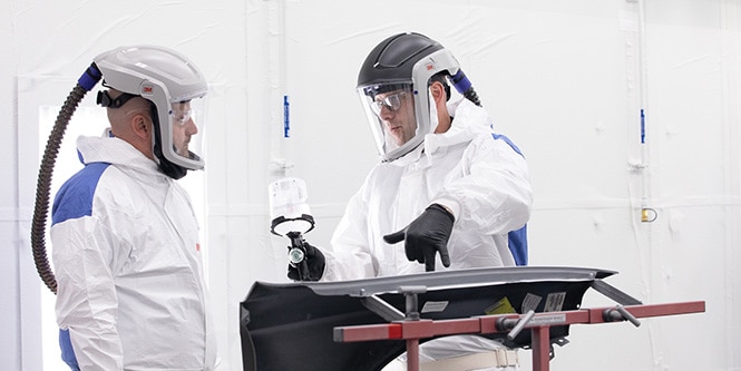 instructor holding paint spray gun and teaching student
