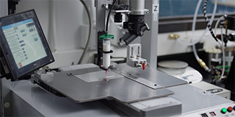 Video still of an automated arm-and-table mechanism applying adhesive
