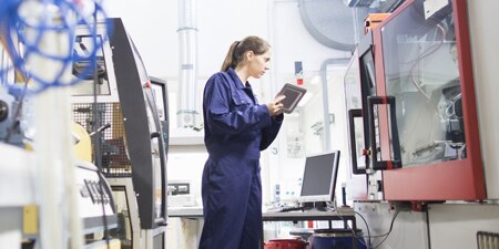 An employee works on industrial equipment with a tablet.
