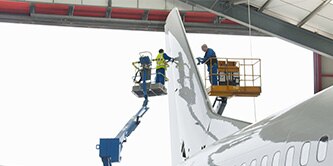 Two people on risers inspecting an aircraft tail.