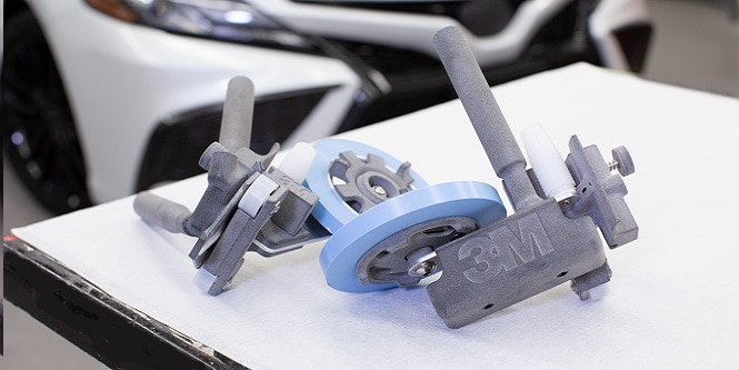 Image of 3MTM Adjustable Paint Masking Applicator resting on a table with a car in the background.
