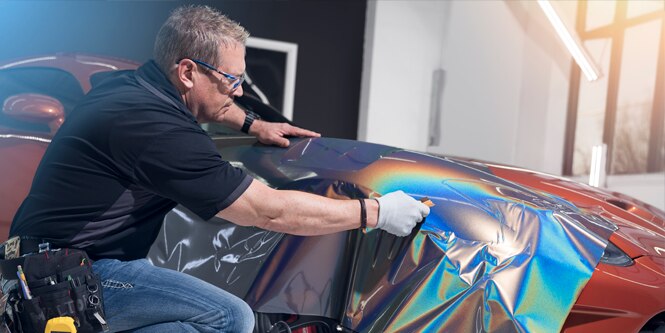 two men installing an orange wrap film on a car

