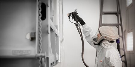 Person wearing ppe using a paint sprayer on a military land vehicle
