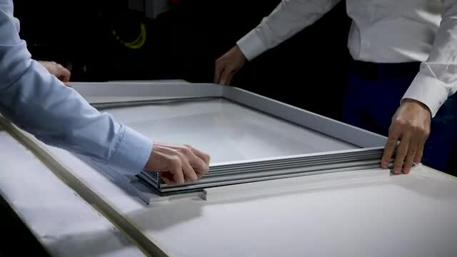 Video still of two workers placing a frame on a plate of glass to which 3M™ VHB™ Extrudable Tape GP has been applied.
