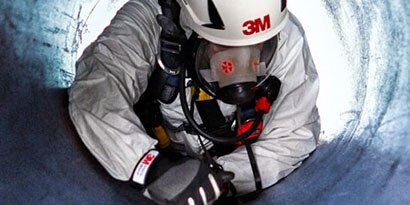 A worker wearing breathing apparatus descending into a confined space.
