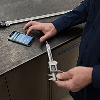 Worker entering information from calipers into app on smartphone