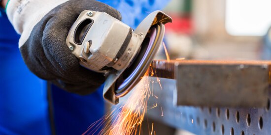 Person grinding metal with a hand held grinder with sparks being emitted.
