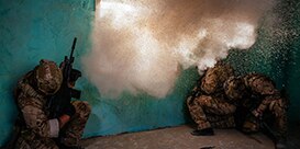 swat personnel in room with window being blown out
