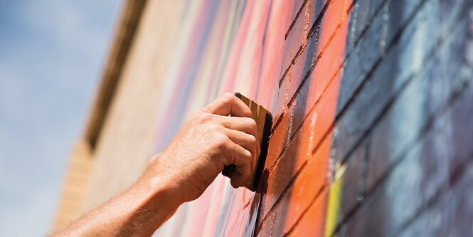 Close of hand using tool to install printed graphic film on brick wall
