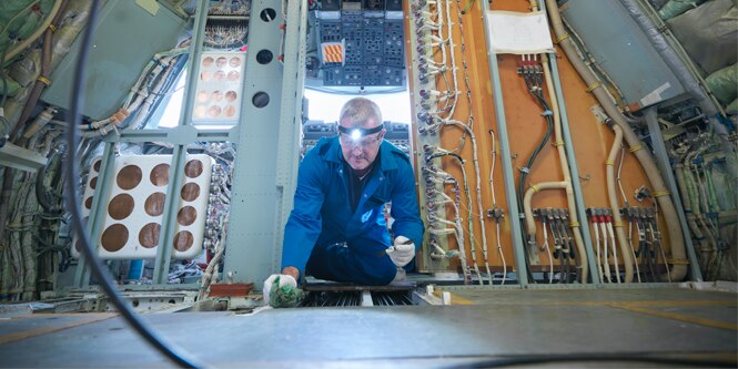 Man applying sealant to the floor and braces in the aircraft fuselage lodge.
