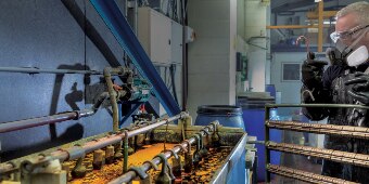 Image of a worker in protective gear preparing to hang a rack of parts in an electroplating bath
