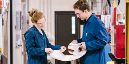 Two technicians in blue lab coats inspecting a product.
