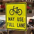Yellow road sign with image of bicycle and words “may use full lane.”
