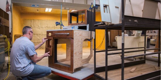 Man in his workshop sanding off unwanted compounds from a piece of handmade furniture.
