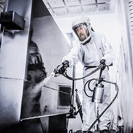 Person in a lab in a full body white suit spraying something.