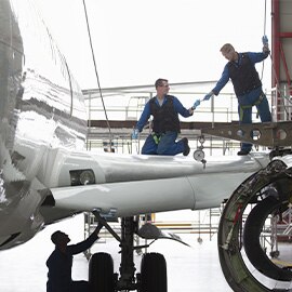 Two people working on an aircraft wing in a hangar.