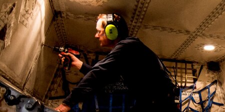 Man using eye and hearing protection while drilling into a wall.
