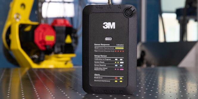 3M Adhesive Mix Monitor sits on a table with machinery in the background. 
