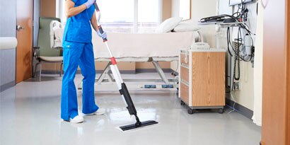 Hospital worker mopping the floor of a hospital patient room.
