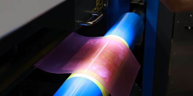 Close-up of a pink flexographic printing plate being mounted onto a blue cylinder with the 3M logo visible.
