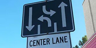 Stacked road signs, one depicting two driving lanes and one turn lane, and the other with the words “center lane.”
