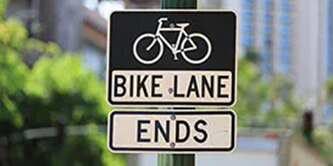 Black and white signs with image of bicycle and words “bike lane ends.”
