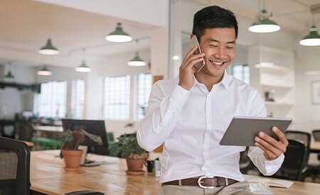 Image of smiling businessman talking on phone and looking at tablet.
