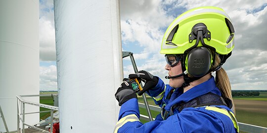 worker on wind tower wearing active hearing protection and safety helmet
